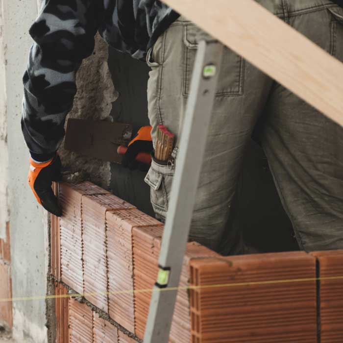 Bricklayer installing brick masonry on interior wall.